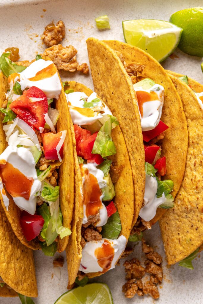 close up of Easy turkey Tacos assembled with seasoned ground turkey, fresh veggies, dairy-free sour cream, hot sauce, and crunchy shells