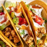 close up of Easy turkey Tacos assembled with seasoned ground turkey, fresh veggies, dairy-free sour cream, hot sauce, and crunchy shells