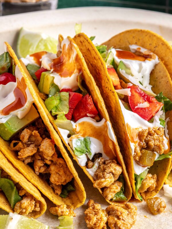 close up of Easy turkey Tacos assembled with seasoned ground turkey, fresh veggies, dairy-free sour cream, hot sauce, and crunchy shells