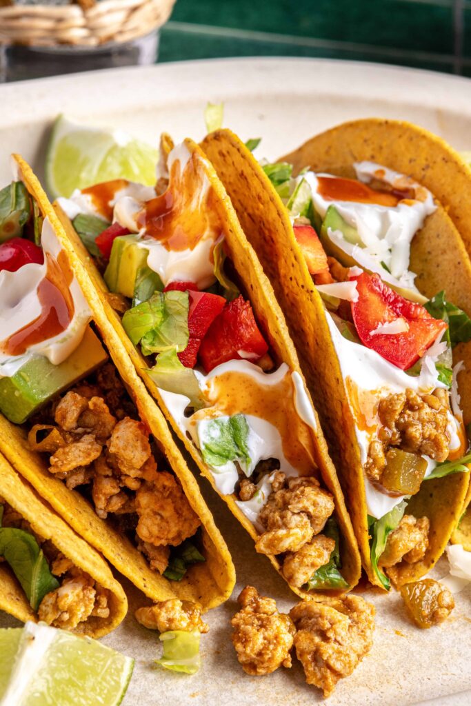 close up of Easy turkey Tacos assembled with seasoned ground turkey, fresh veggies, dairy-free sour cream, hot sauce, and crunchy shells