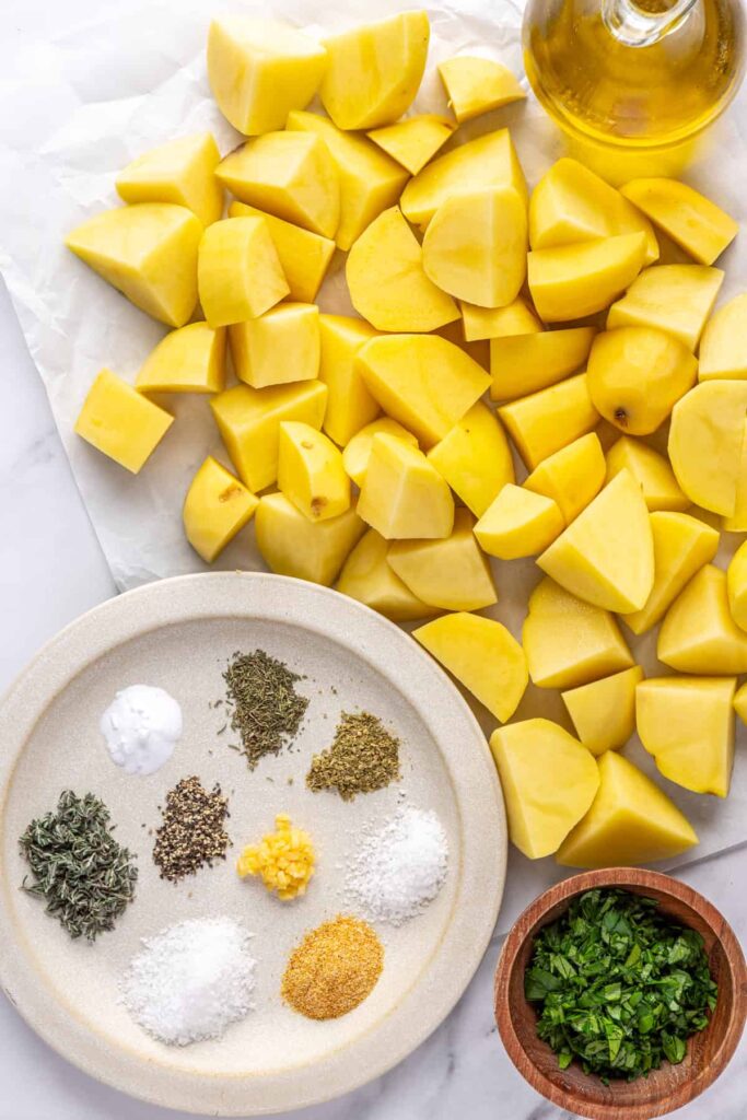 Ingredients for crispy English roast potatoes including Yukon gold potatoes, olive oil, herbs, garlic, and parsley