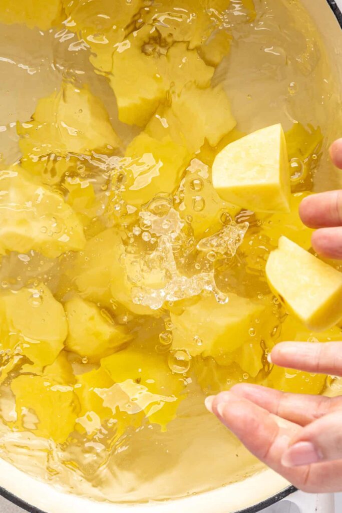 close up of cubed Yukon gold potatoes being added to a pot of water to make English roast potatoes