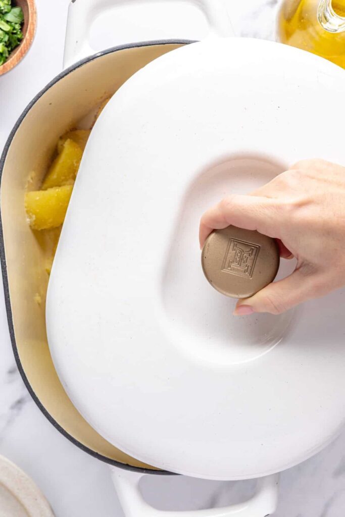 overhead shot of the lid being placed on top of the stockpot to cover the english roast potatoes, before giving them a shake