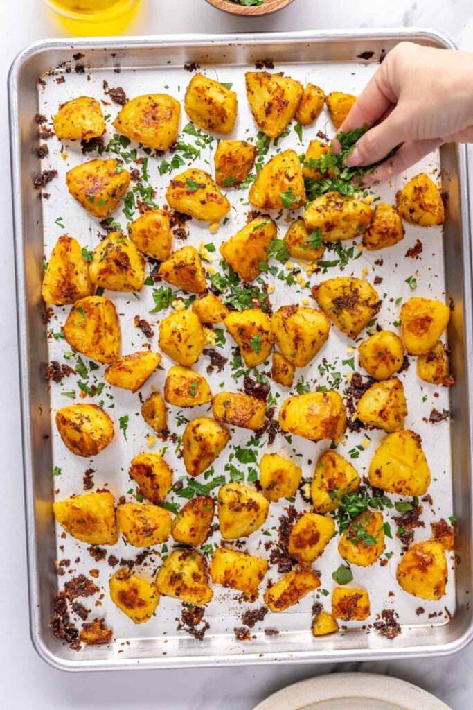 Garnishing crispy English roast potatoes with fresh parsley and garlic
