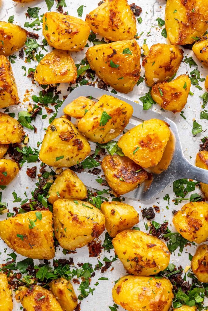 close up of spatula scooping crispy English roast potatoes from baking sheet