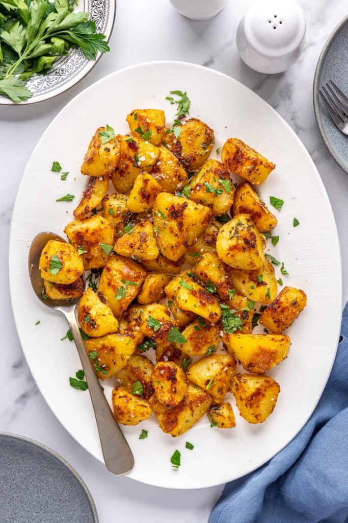 Crispy English roast potatoes served on a white platter with fresh herbs