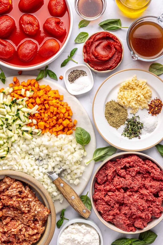 Overhead shot of ingredients for creamy homemade vodka sauce with hidden veggies, including tomatoes, onion, zucchini, carrot, garlic, and herbs