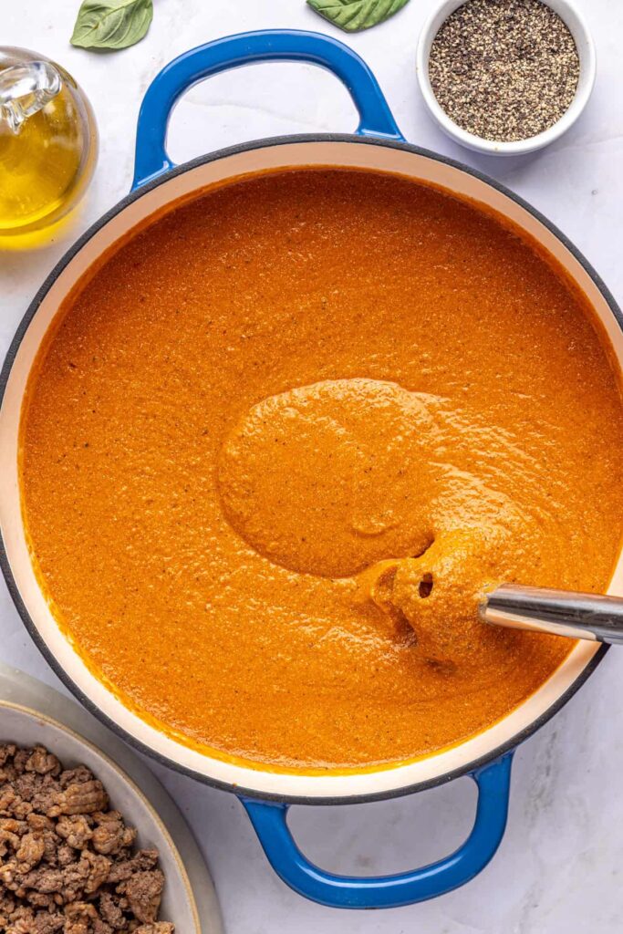 Immersion blender pureeing hidden veggie vodka sauce until smooth, overhead shot