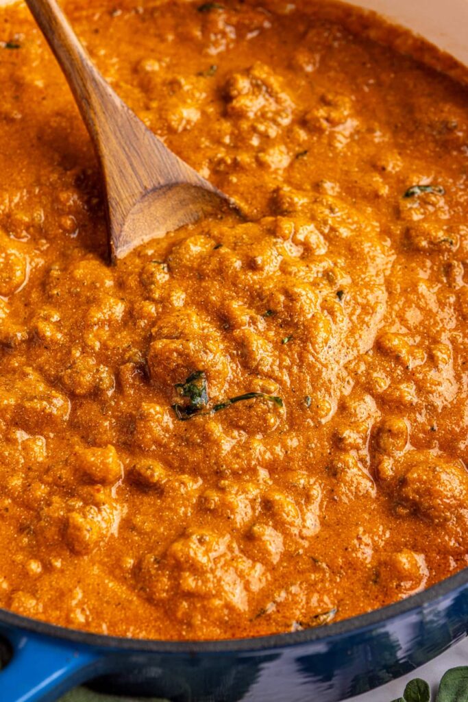 Close-up overhead shot of creamy homemade vodka sauce in a Dutch oven with a wooden spoon