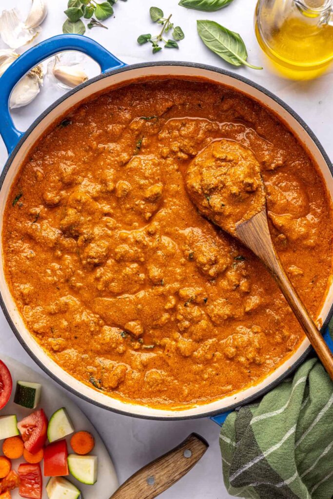 Overhead view of finished creamy homemade vodka sauce in a Dutch oven with a wooden spoon