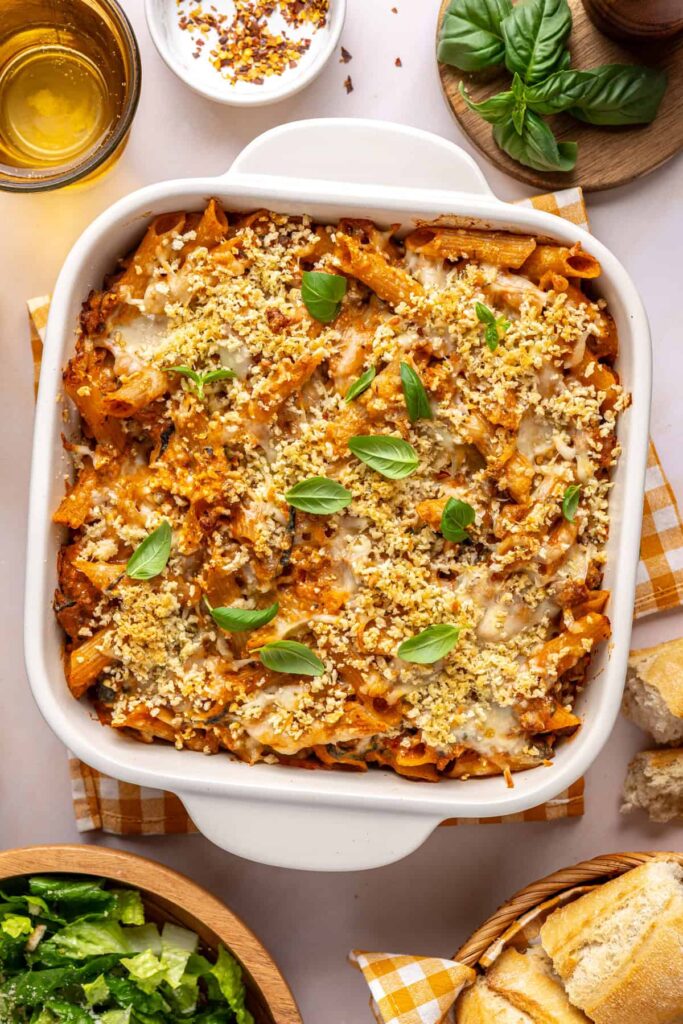 Overhead view of easy baked ziti in a white baking dish with basil and toasted baguette
