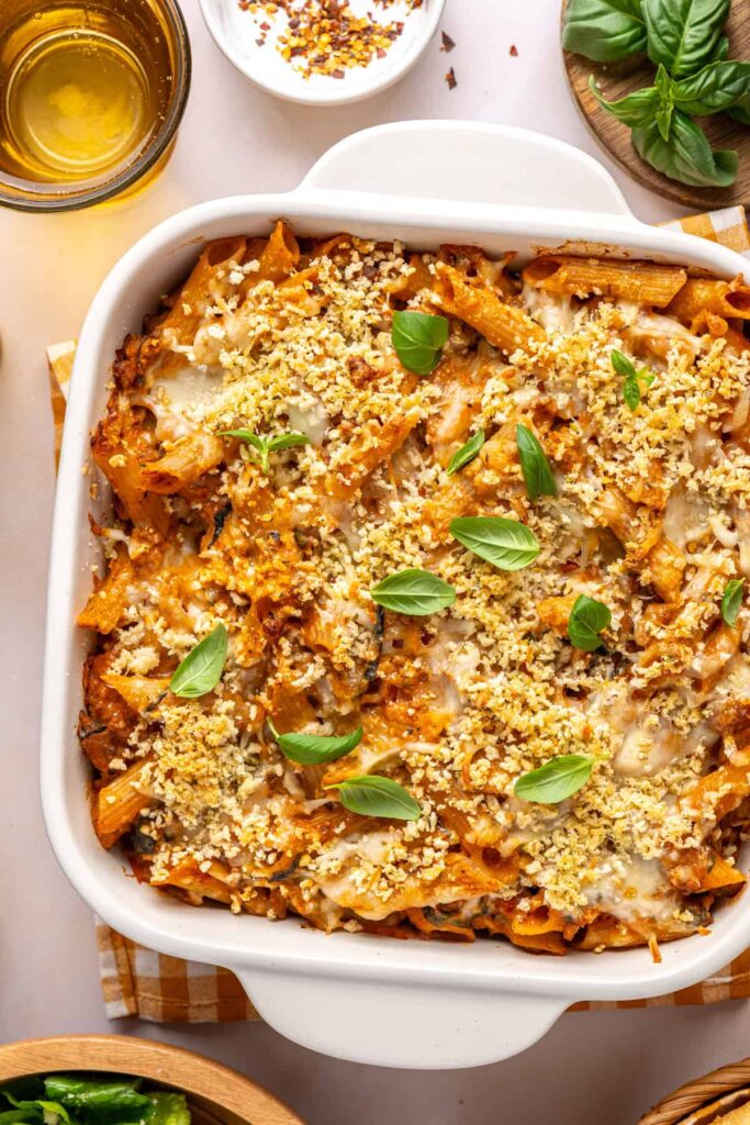 Overhead view of easy baked ziti in a white baking dish with basil and toasted baguette