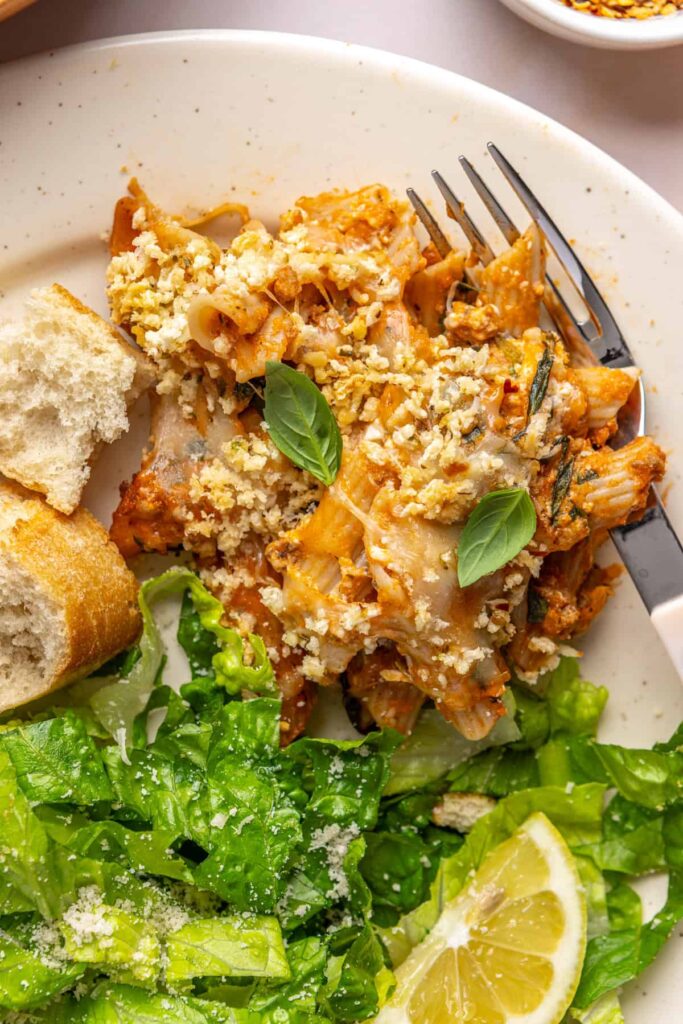 Easy baked ziti served on a plate with side salad and toasted baguette
