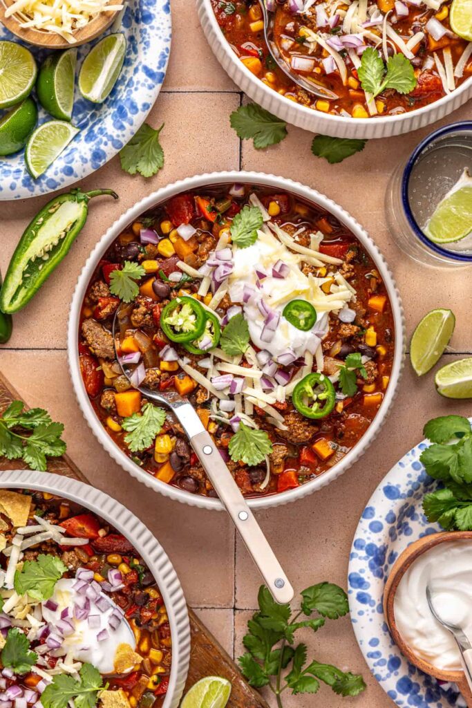 Hearty chipotle beef & black bean soup styled with garnishes and a drink nearby