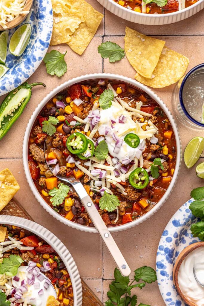 Chipotle beef & black bean soup served with lime wedges and toppings on a styled dinner table
