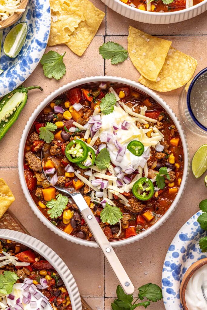 Chipotle beef & black bean soup served with lime wedges and toppings on a styled dinner table