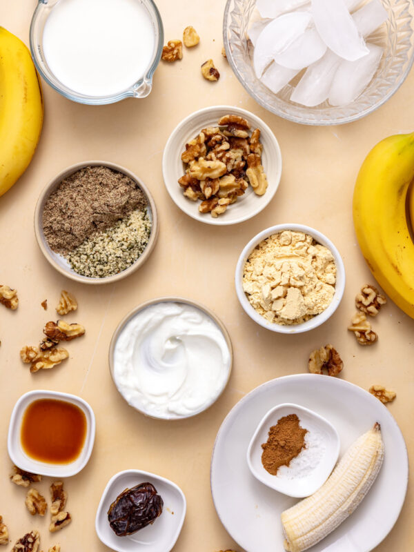 Overhead shot of ingredients for a banana nut smoothie including frozen banana, walnuts, flaxseed, protein powder, almond milk, and yogurt