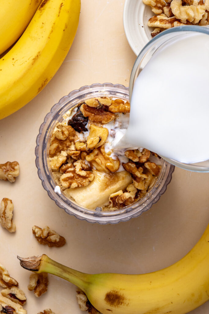 Pouring almond milk and adding coconut yogurt into blender for banana nut smoothie