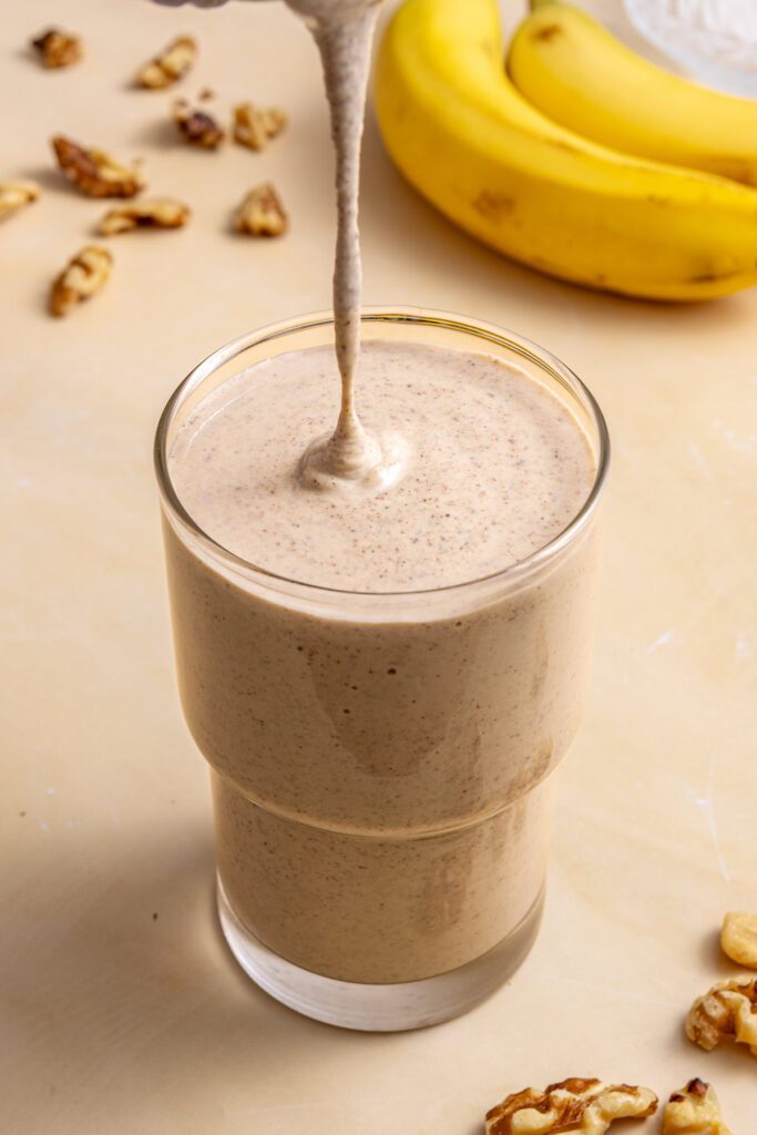 Pouring thick banana nut smoothie into glass from blender