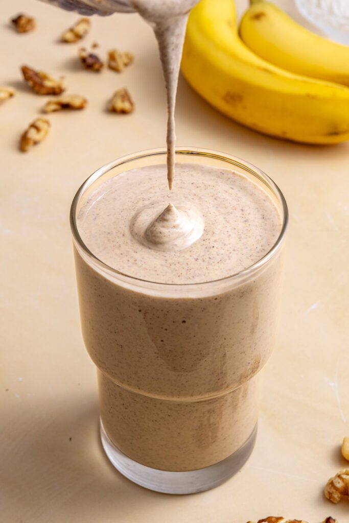 Creamy banana nut smoothie dripping into serving glass during pour