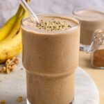 Styled banana nut smoothie on table with smoothie-filled glass and ingredients nearby