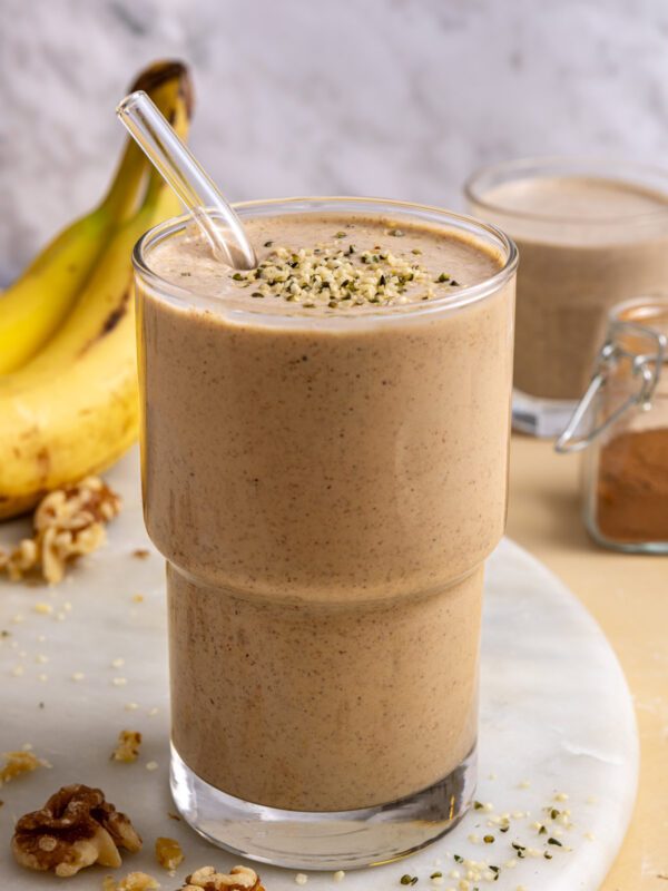 Styled banana nut smoothie on table with smoothie-filled glass and ingredients nearby