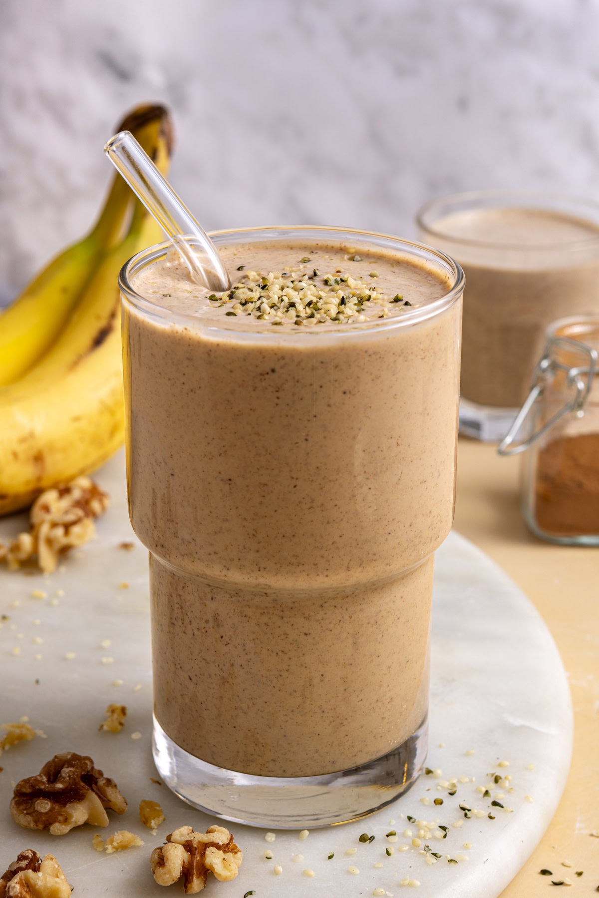 Styled banana nut smoothie on table with smoothie-filled glass and ingredients nearby