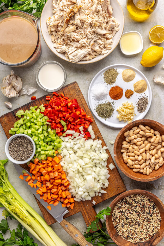 Ingredients for cajun chicken soup arranged overhead, including chicken, wild rice, vegetables, herbs, beans, and broth