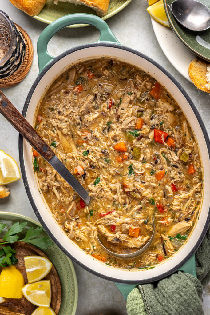 Large pot of creamy cajun chicken soup on table with ladle, crusty bread, and lemon wedges