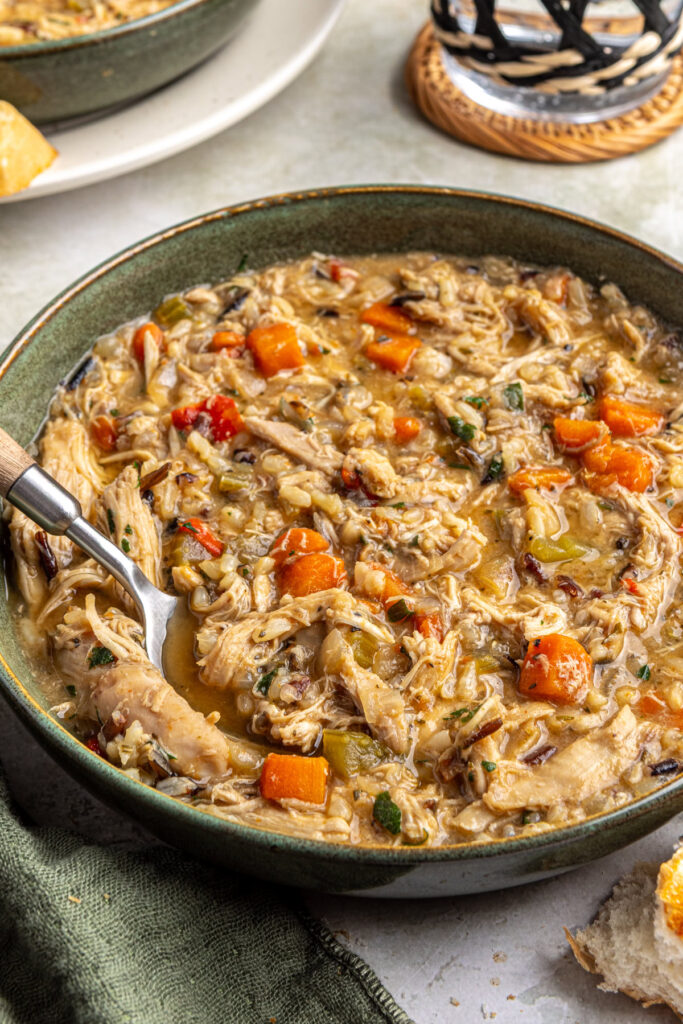 Healthy cajun chicken soup served in bowl next to glass of water on styled table