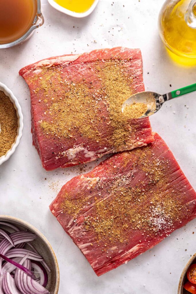 Raw flank steak coated in spices for slow cooker Greek beef bowls