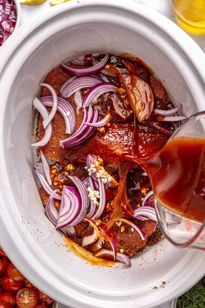 Greek braising sauce poured over seasoned flank steak in a crock-pot
