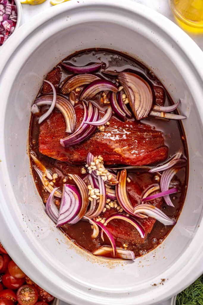 Greek beef bowls ingredients layered in a slow cooker before cooking