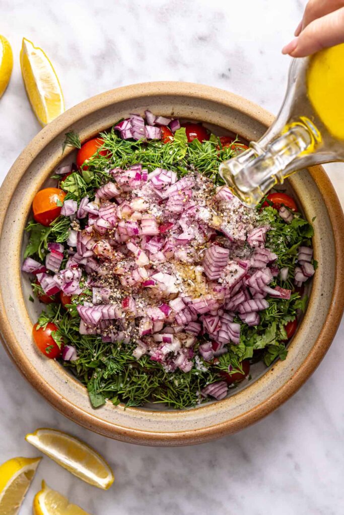 pouring olive oil into fresh tomato relish with herbs and lemon for Greek beef bowls