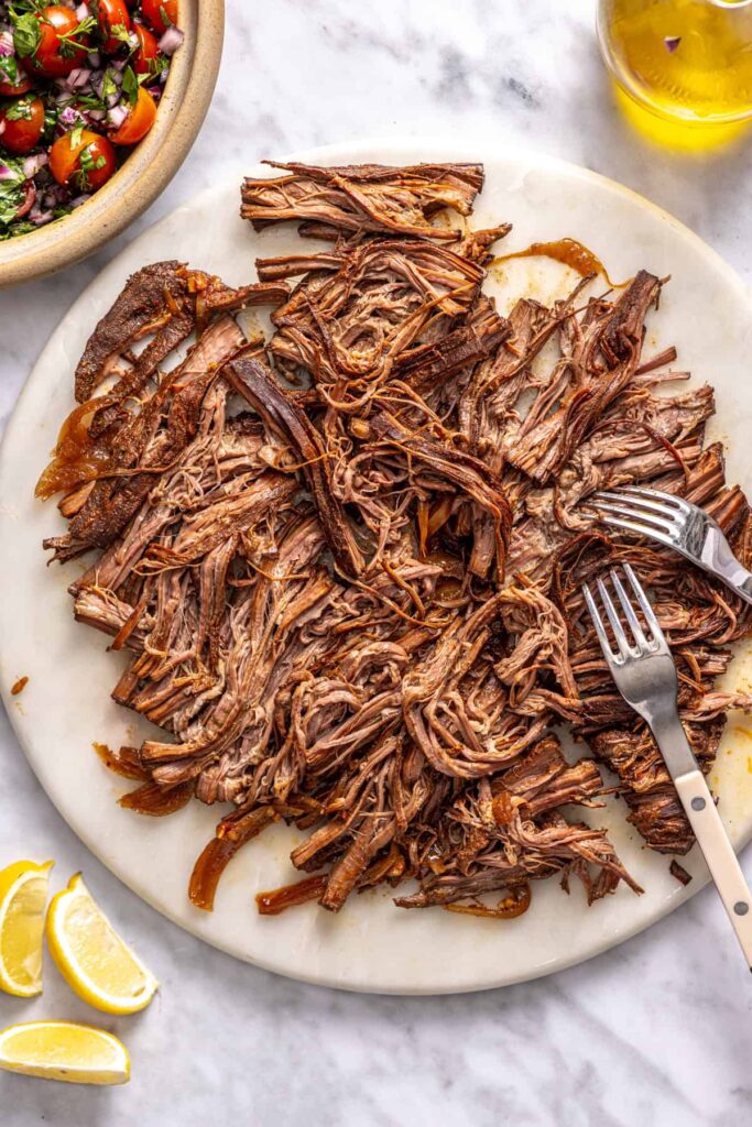 Tender slow-cooked Greek beef being shredded with forks
