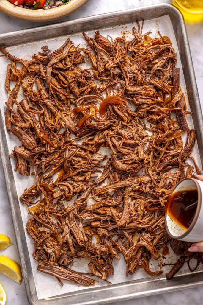 adding the cooking liquid to the cooked and shredded flank steak on a sheet pan