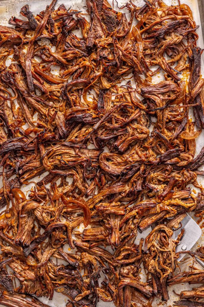 close up of Shredded Greek beef broiled until crispy on a parchment-lined sheet pan
