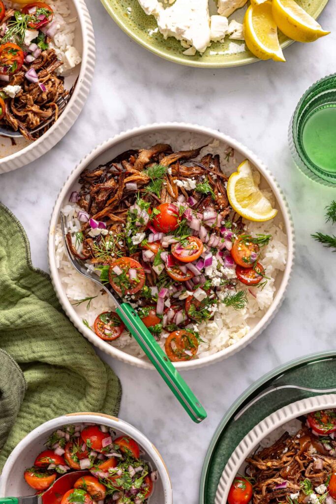 Overhead view of crispy Greek beef bowls with rice, tomato relish, feta, and lemon wedge