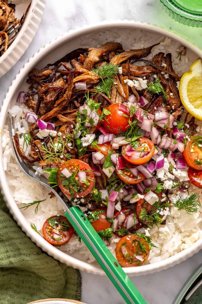 close-up, overhead view of crispy Greek beef bowls with rice, tomato relish, feta, and lemon wedge