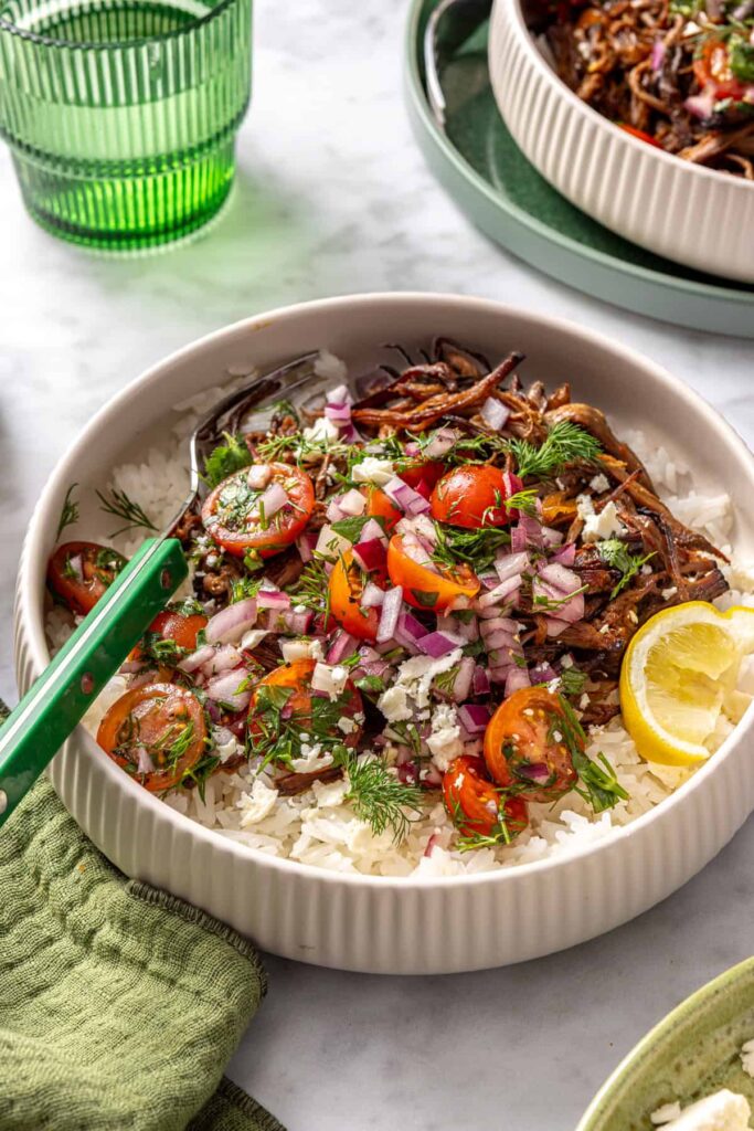 close-up, overhead view of crispy Greek beef bowls with rice, tomato relish, feta, and lemon wedge