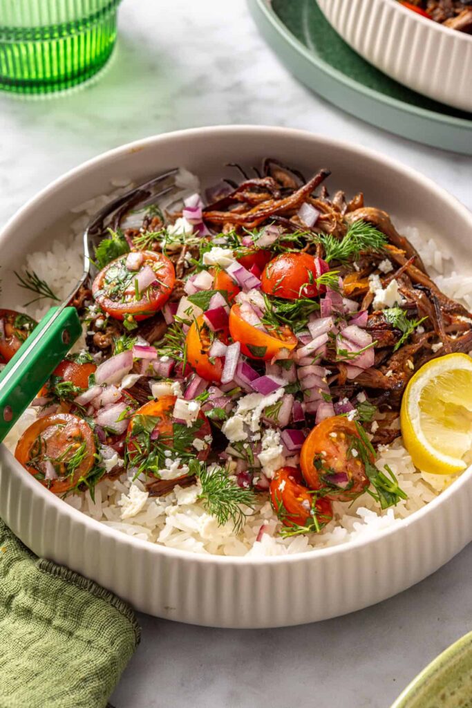 Side view of Greek beef bowl garnished with feta, herbs, and lemon wedge