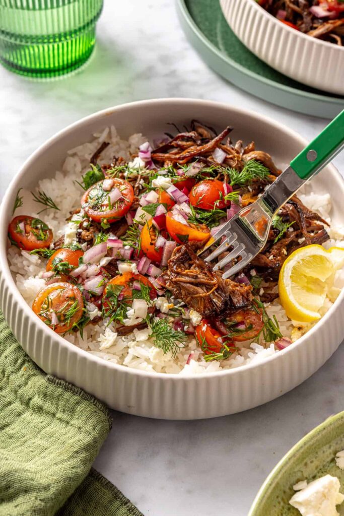 Side view of Greek beef bowl garnished with feta, herbs, and lemon wedge