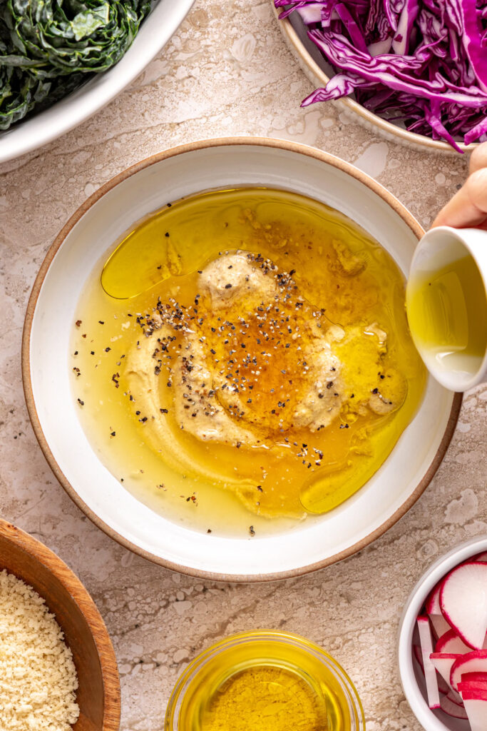 pouring olive oil into a white bowl with other ingredients for homemade honey mustard dressing