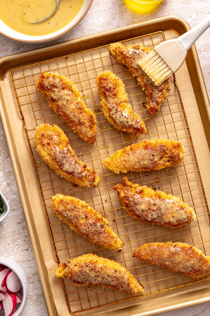 Pastry brush spreading honey mustard over chicken before baking
