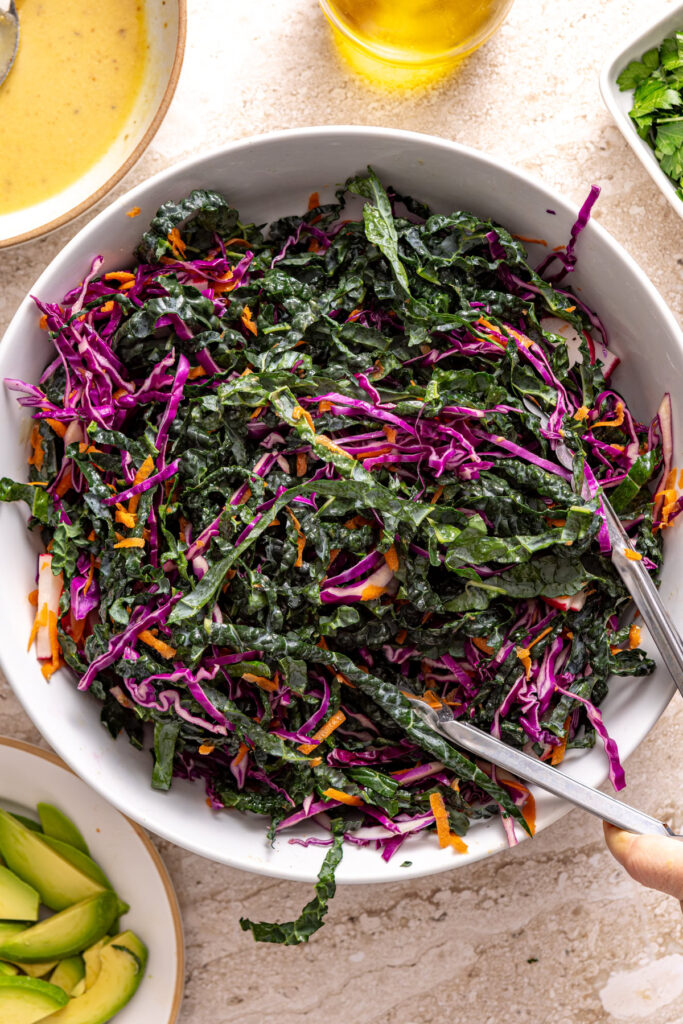 Tossing kale and cabbage with dressing in large bowl