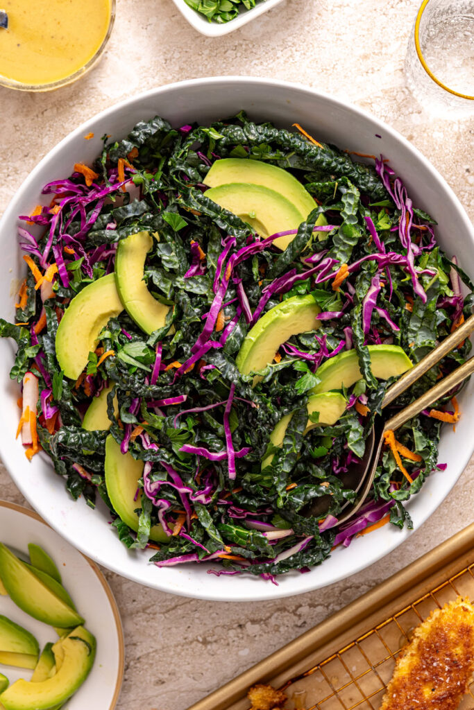Adding sliced avocado to chicken kale salad