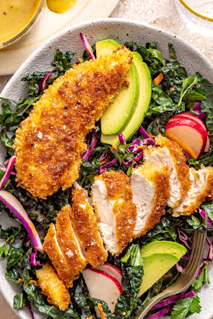 Sliced crispy chicken placed over massaged kale salad