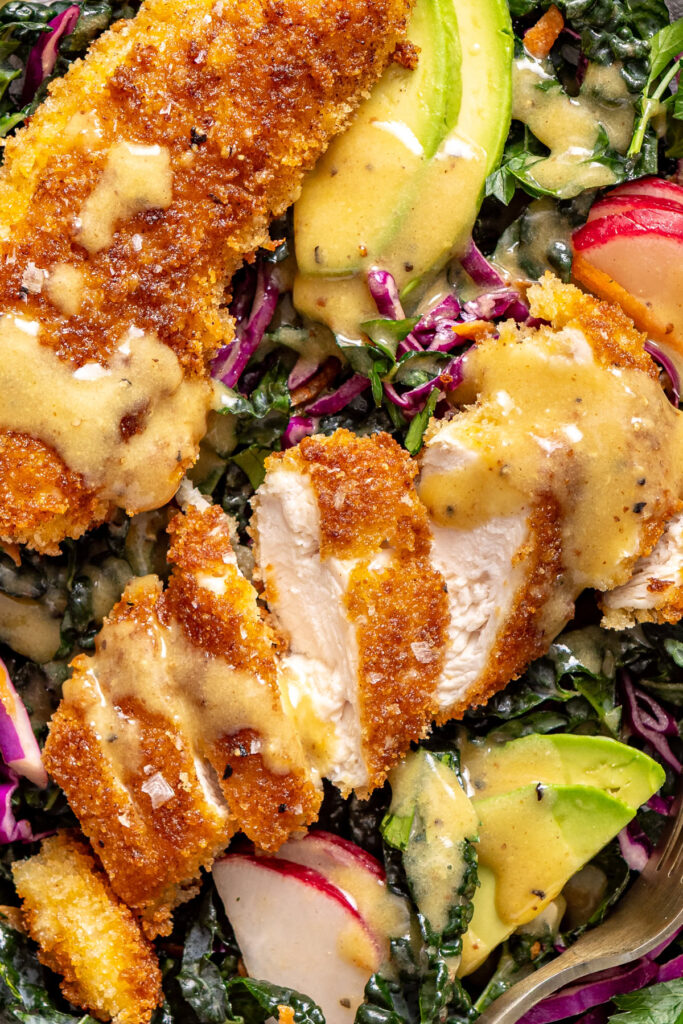Close-up detail of sliced crispy chicken on kale salad with avocado