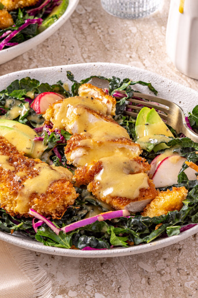Crispy chicken kale salad with avocado, cabbage, and radishes drizzled with honey mustard dressing