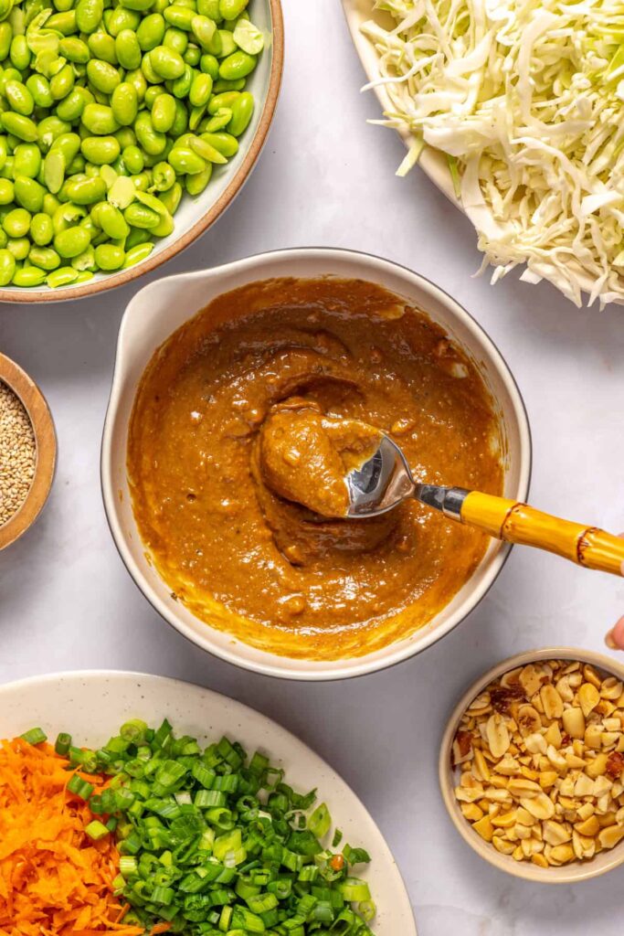Homemade sesame peanut dressing being stirred with a spoon in a small bowl